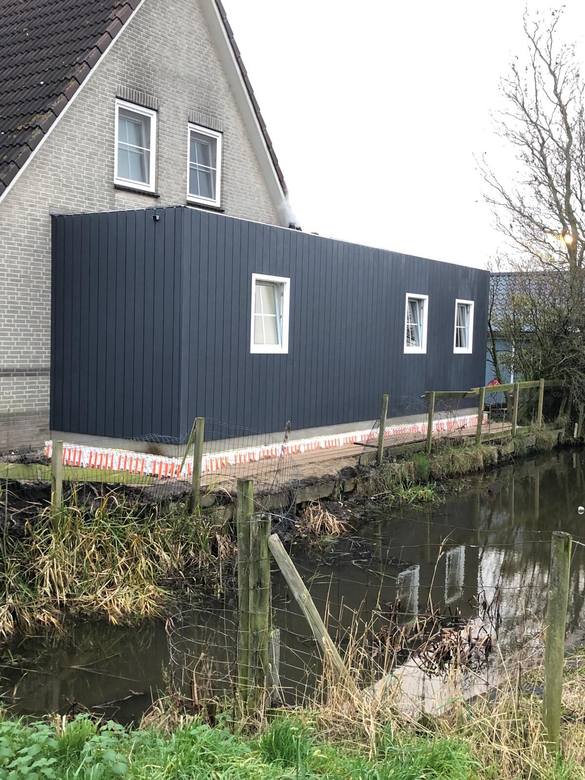 Aanbouw met zwarte gevel aan een woning aan het water, door LBH Bouw