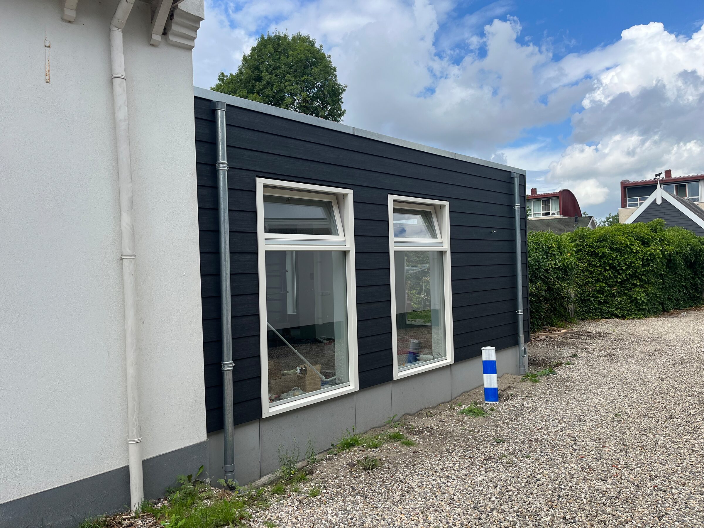 Aanbouw met zwarte gevel naast een wit huis, door LBH Bouw